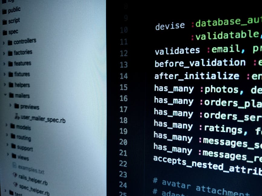 A close-up photograph of a laptop computer displaying lines of programming code on its dark screen, with syntax highlighting in green, blue, and pink. The laptop is positioned on a wooden surface, and